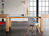 Tavolo Alta Corte modello Sidney. Il tavolo ha il piano in vetro trasparente e la struttura in legno rovere disponibile in diverse finiture.